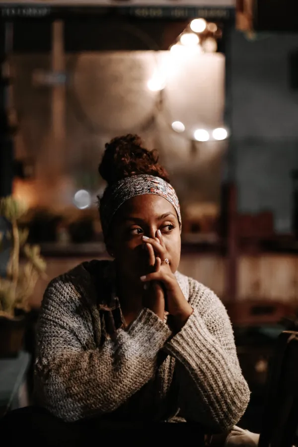 woman sitting in cafe looking contemplative with hands covering her face